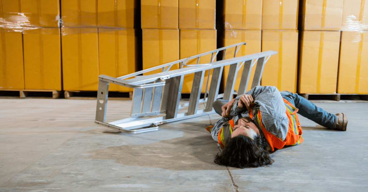 Injured warehouse worker lying on the ground next to a fallen ladder, wearing a safety vest and surrounded by shipping boxes.