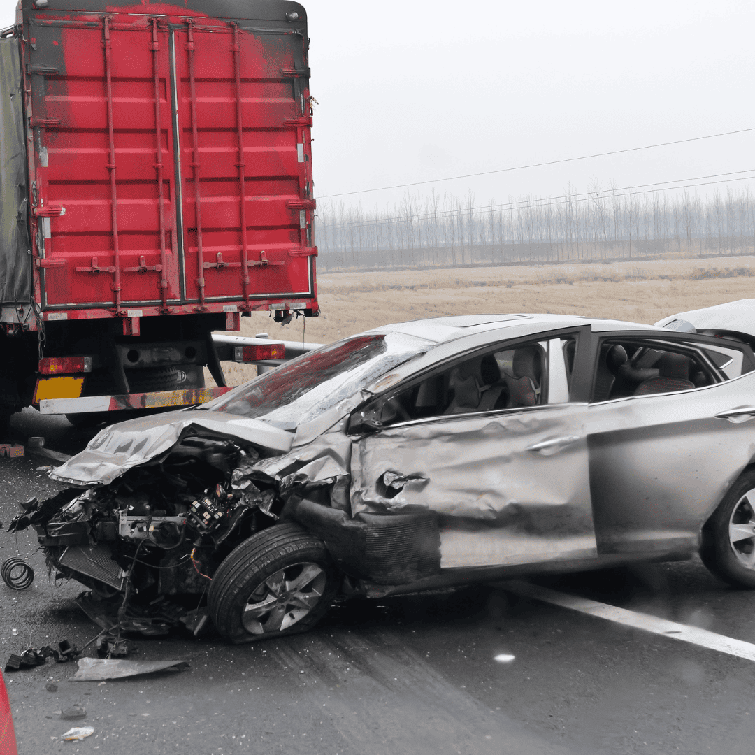 Crumpled passenger car after a collision with a large red semi-truck on a rural highway