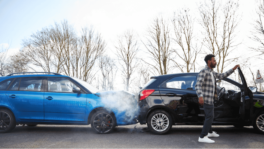 Man standing next to his car after a rear-end collision with another vehicle on a sunny road
